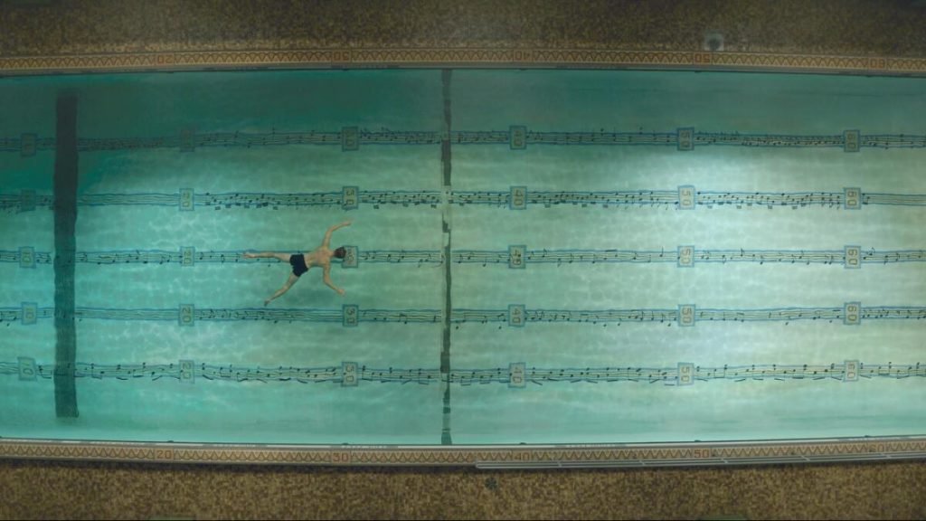 Jonathan Larson (Andrew Garfield) nadando en una piscina mientras flota una partitura musical. Escena de la película "Tick, Tick...Boom!", dirigida por Lin-Manuel Miranda (2021)