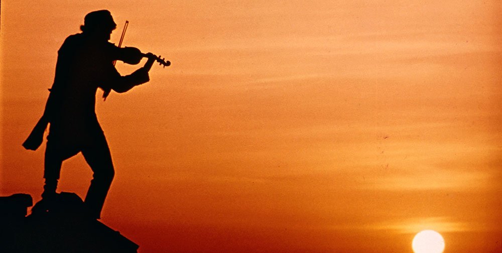 Chaim Topol tocando el violín en el atardecer en la adaptación cinematográfica de "El Violinista en el tejado".